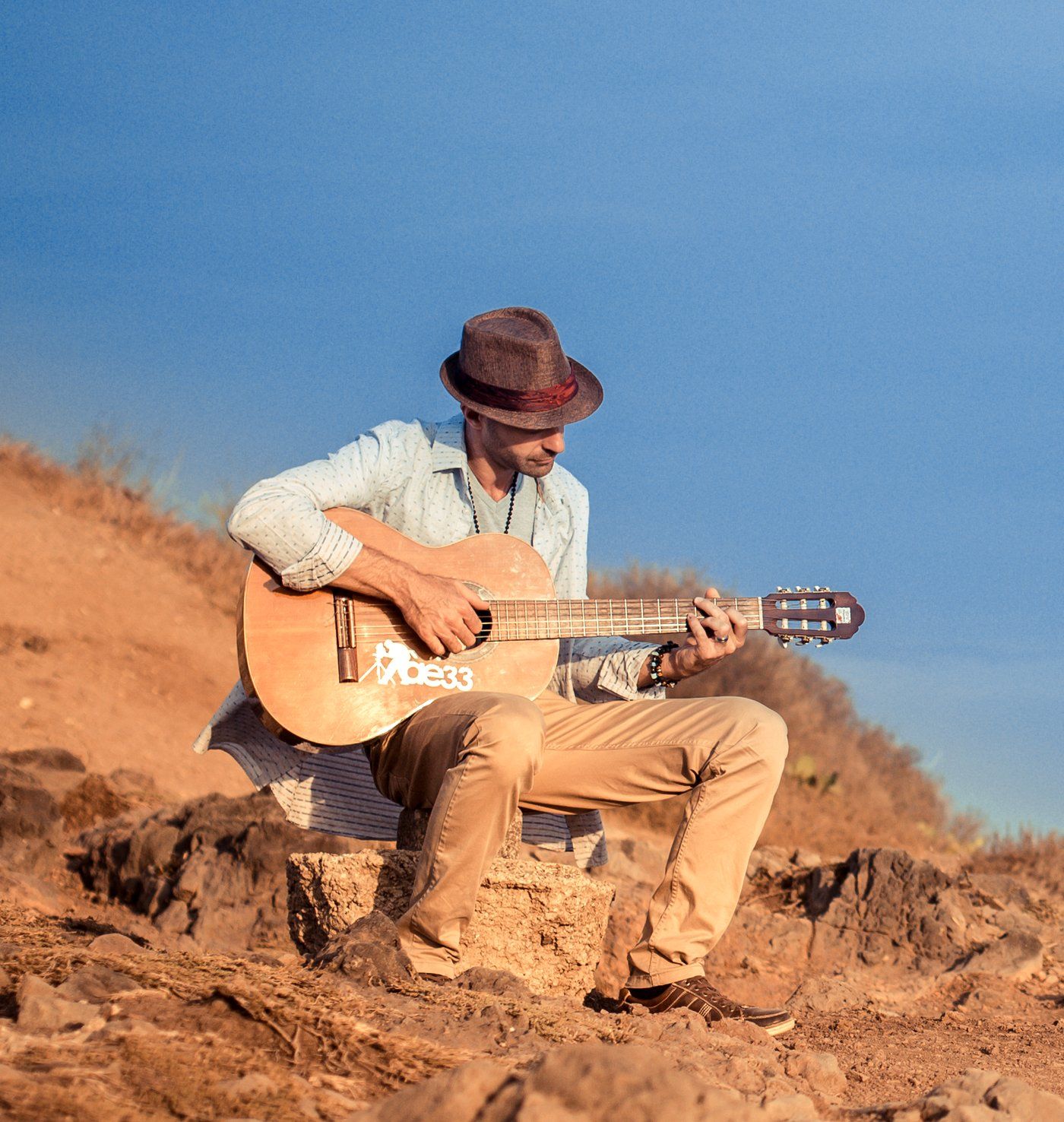 Cédric B. assis sur la roche face à la mer, guitare classique en main