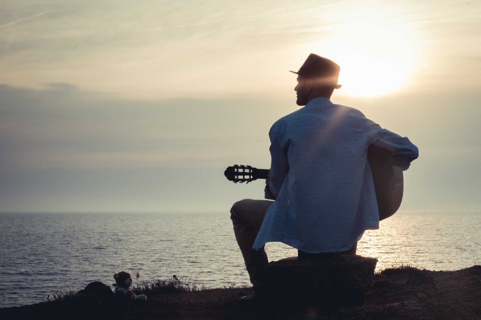 Cédric B. assis face à la mer au coucher du soleil, guitare à la main